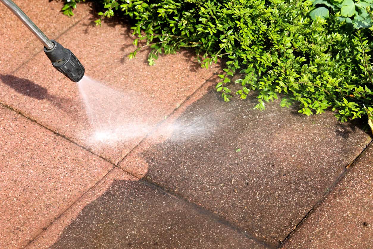 Pressure washing removing dark surface dirt from paving slabs